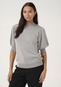 Pull en tricot gris clair avec un col montant, des manches bouffantes courtes et une finition texturée, associé à un pantalon noir. Design simple et moderne.