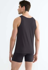 Donkergrijze tanktop met een ronde hals, zachte textuur en een aansluitend ontwerp, gecombineerd met zwarte shorts, gezien vanuit de achterkant.