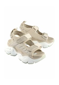 Sandales beiges avec des sangles ajustables, semelle rembourrée et épaisse semelle blanche. Présente un détail de logo, un mesh respirant et un dessus texturé.