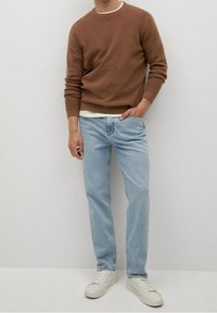 Brązowy dziergany sweter, jasnoniebieskie jeansy i białe trampki. Sweter ma okrągły dekolt i długie rękawy; jeansy są proste z widocznym przeszyciem.