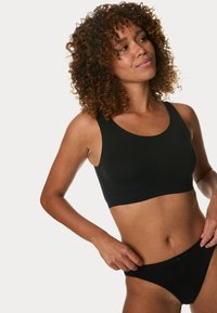 Svart sömlös bralette med breda axelband och rundad halsringning, kombinerad med svarta bikinistilunderkläder med en liten rosett detalj.