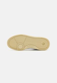 Sålen på en sneakers, med et teksturert gummimateriale i lys beige med et sikksakkmønster og sirkulært merke.
