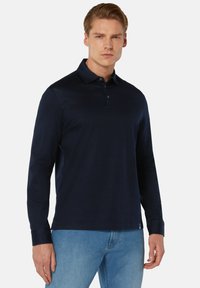 Marineblauw polo shirt met lange mouwen, kraag, knoopsluiting en een gladde textuur, gecombineerd met lichtblauwe spijkerbroek.