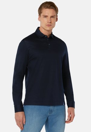 Marineblauw polo shirt met lange mouwen, kraag, knoopsluiting en een gladde textuur, gecombineerd met lichtblauwe spijkerbroek.