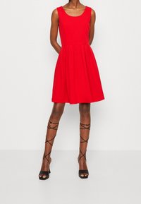 Robe sans manches rouge avec un corsage ajusté et une jupe évasée. Portez-la avec des escarpins noirs à brides, présentant une texture lisse et un design minimaliste.