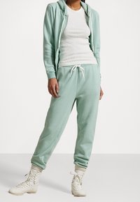 Mintgrön huvtröja med vita dragsnören, matchad med joggers i samma färg med dragsnöreliv. Texturerad tyg och ribbade ärmslut.