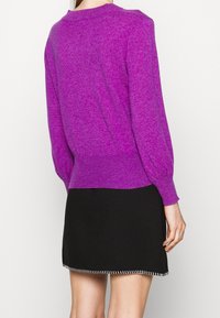 Pull tricot violet à manches longues et ourlet côtelé, associé à une jupe noire avec un accent blanc surpiqué en bas.