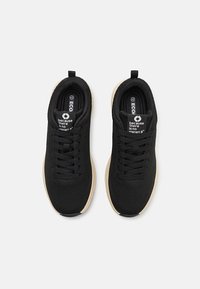 Chaussures de sport noires en mesh respirant avec une semelle beige rembourrée. Équipées de lacets et d'un logo sur la languette, conçues pour le confort et la performance.