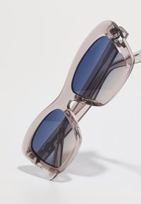 Oversized sunglasses with a transparent mauve frame and gradient blue lenses; features subtle branding and a smooth, glossy texture.