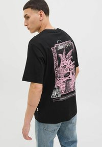 Sort bomulds T-shirt med et stort pink grafisk print på ryggen, med stiliserede planter og tekst. Korte ærmer og afslappet pasform.