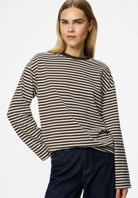 Dug drugi majica dugih rukava sa horizontalnim smeškim i belim prugama, mekim materijalom, opuštenim krojem i okruglim izrezom. Uparena sa tamnim farmerkama.