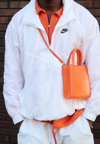 Vit lättviktsjacka med dragkedja, orange detaljer och logotyp; tillsammans med en orange mini-väska med slät yta och korta handtag.