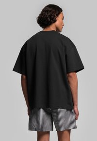 Svart oversized t-shirt med korta ärmar, tillverkad av bomull, ihopparat med randiga shorts. Synliga sömdetaljer, avslappnad passform.