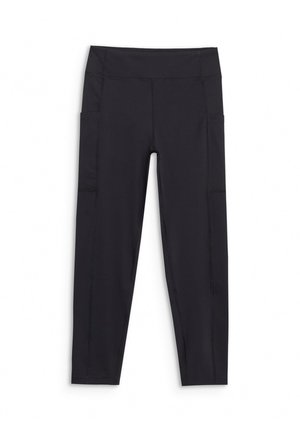 Jeune personne debout portant un t-shirt graphique rose, des leggings noirs et des chaussures de randonnée noires sur un fond clair uni.