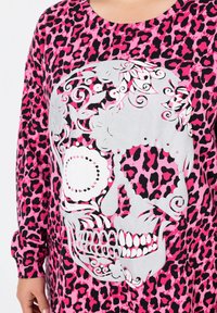 Langärmliges Oberteil mit einem pinken Leopardenmuster, einem großen silbernen Totenkopf-Graphic, komplizierten Mustern und kontrastierenden weißen Akzenten.