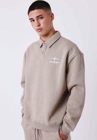 Felpa beige oversize con design a collettino, caratterizzata da un logo "PXP" bianco e polsini a costine. Il tessuto sembra morbido e con una texture interessante.