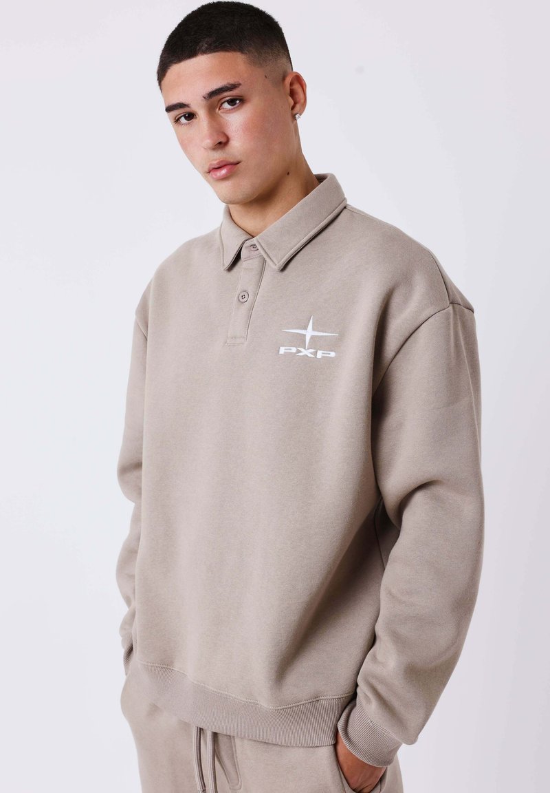 Felpa beige oversize con design a collettino, caratterizzata da un logo "PXP" bianco e polsini a costine. Il tessuto sembra morbido e con una texture interessante.