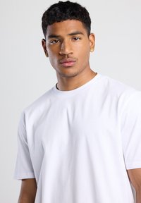 T-shirt en coton blanc à manches courtes avec un col rond. Texture lisse et coupe décontractée, avec des détails de couture subtils.