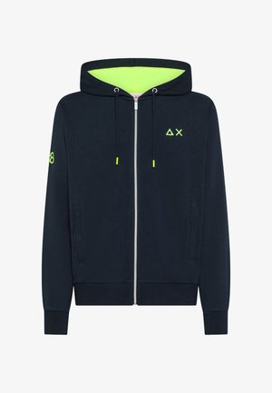 Felpa con cappuccio con zip color blu navy, con interno del cappuccio verde neon, estremità del cordino, piccolo logo a triangolo e X sul petto, e numero 8 sulla manica sinistra.