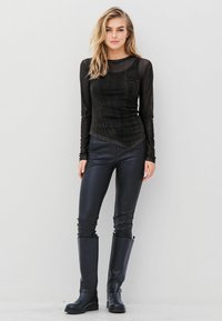 Sort langærmet top med en tekstureret finish, parret med slanke sorte fake læderbukser og knæhøje sorte støvler.