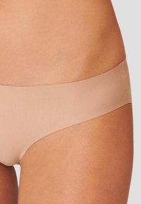 Nudefarbene nahtlose Bikini-Unterwäsche mit dünnem elastischem Bund, glatter Textur und minimaler Abdeckung, ideal für diskretes Tragen unter der Kleidung.