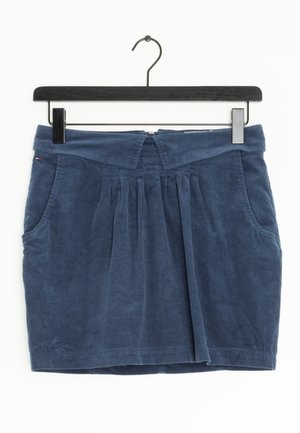 Mini-jupe en velours côtelé bleu marine avec plis sur le devant, poches latérales et ceinture pliée, suspendue sur un cintre noir.