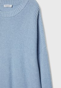 Pull tricoté bleu clair avec col rond côtelé et manches longues, étiquette Stradivarius, fabriqué au Bangladesh.
