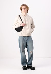 Crèmefarvet bomberjakke, slidte lyseblå jeans, sorte platform sko og en sort crossbody taske. Simpel, afslappet design med synlige revner.