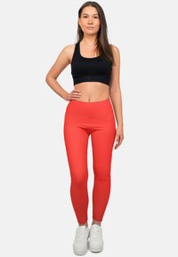 Rode leggings van rekbare stof met een hoge taille. Gepaard met een zwarte crop top en witte sneaker. Gladde textuur.