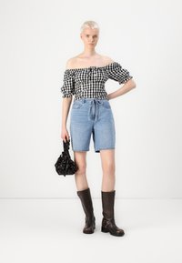 Off-the-shoulder black and white gingham blouse with puffed sleeves, paired with high-waisted denim shorts and knee-high brown boots.