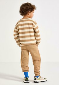 Gestreifter beige und cremefarbener Pullover, passende beige Sweatpants und mehrfarbige Sneakers. Weicher Stoff und lockere Passform mit Bündchen an den Hosen.