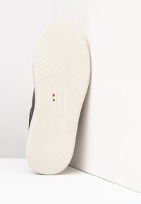 Czarny sneakers z teksturowaną cholewką i białą gumową podeszwą z geometrycznym wzorem. Rozmiar 37 z widocznym logo na podeszwie.