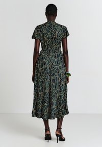 Robe maxi de couleur vert foncé avec un motif de feuilles jaunes, manches courtes évasées, taille élastique et jupe plissée. Dotée d'une silhouette fluide.