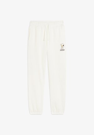 Pantaloni della tuta color crema con cintura elasticizzata, cordino e polsini a costine. Presentano una grafica di Snoopy sulla coscia sinistra.