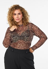 Dugi rukav top izrađen od prozirnog materijala s printom leopard uzorka u smeškim i crnim tonovima, uparen s crnim hlačama visokog struka s detaljima od dugmadi.