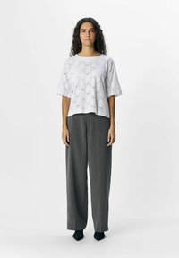 Haut blanc à manches courtes avec des motifs découpés complexes, associé à un pantalon ample de couleur gris charbon. Tissu texturé et coupe décontractée.