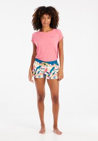 Maglietta rosa a maniche corte con logo e pantaloni corti a fantasia con foglie colorate. I pantaloni corti hanno una vita elastica blu e un cordoncino.