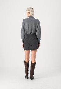 Siva majica z dolgimi rokavi v kombinaciji s črno denim mini krilo z okrasnimi žebljički. Model nosi rjave kavbojske škornje s koničastimi prsti.