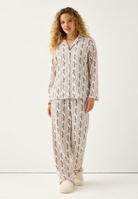 Blomstret pyjamas sæt med lange ærmer og lige bukser, lavet af blødt stof med en hvid baggrund og indviklede røde og grønne mønstre.