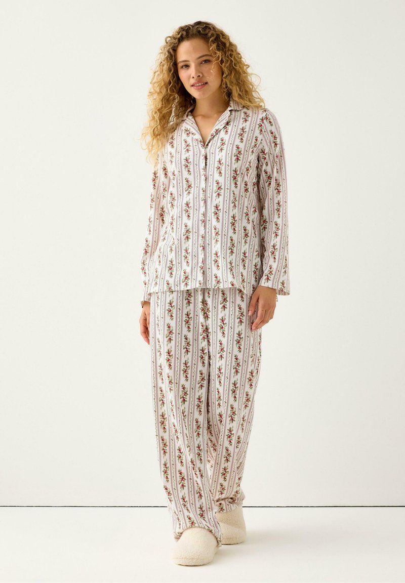 Blomstret pyjamas sæt med lange ærmer og lige bukser, lavet af blødt stof med en hvid baggrund og indviklede røde og grønne mønstre.