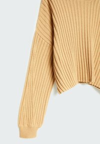 Manche de pull beige en maille côtelée et détail latéral avec poignet et couture d’épaule descendue sur un fond clair.