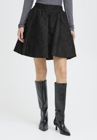 Black skirt with textured rose pattern, elastic waistband, and a flared shape. Paired with high, glossy black knee-length boots.
