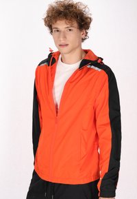 Orange og sort lynlåsjakke med hætte, reflekterende detaljer, letvægtsmateriale og tætsiddende design.