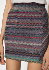 Falda corta y ajustada con un patrón en zigzag en colores metálicos, que incluyen rojo, púrpura y verde, con una tela texturizada y brillante.