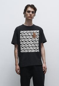 Sort bomulds t-shirt med et grafisk design, der har gentagne stormtrooper ansigtstræk og en fremtrædende Chewbacca figur i midten.