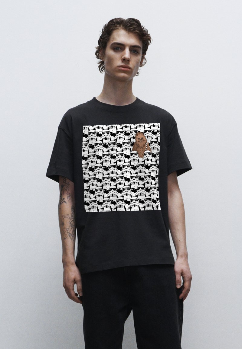 Sort bomulds t-shirt med et grafisk design, der har gentagne stormtrooper ansigtstræk og en fremtrædende Chewbacca figur i midten.