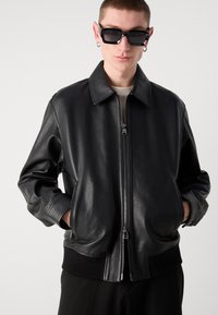 Schwarze Leder-Bomberjacke mit Reißverschluss vorne, umgeschlagenem Kragen und geripptem Saum. Verfügt über Seitentaschen und eine weiche, strukturierte Oberfläche.