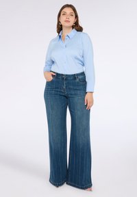 Světle modrá košile s dlouhými rukávy a denimu široké nohavice s vertikálním švem. Oblečení zahrnuje středně vysoký pas a kapsy.