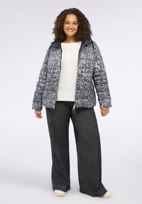 Giacca piumino trapuntata in grigio e blu marino con cappuccio, caratterizzata da una chiusura zip frontale e polsini elastici. Indossata con pantaloni scuri e scarpe chiare.