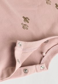 Rosa Baumwollbluse mit weicher Textur, metallischen Druckknöpfen am Ausschnitt und einem Kaktusdruck in Dunkelgrün.